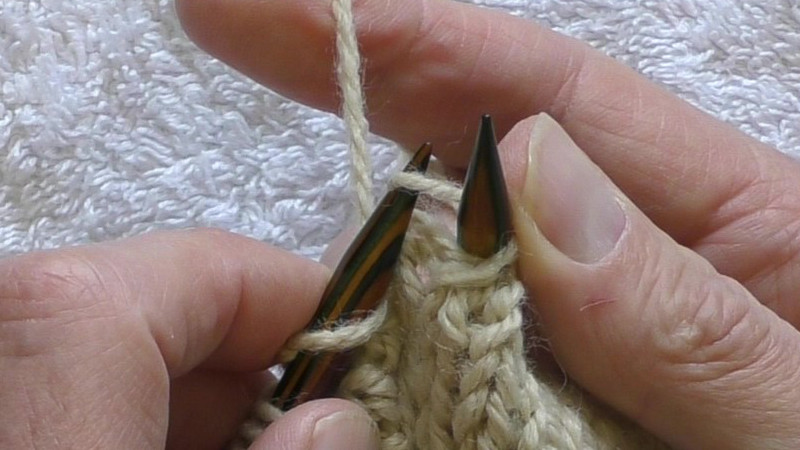 Left hand needle being put through the stitch on the right hand needle. The left (back) leg of the stitch has been placed to the back left of the left hand needle, with the stitch then passing in front of that needle. The yarn is held behind the fabric.