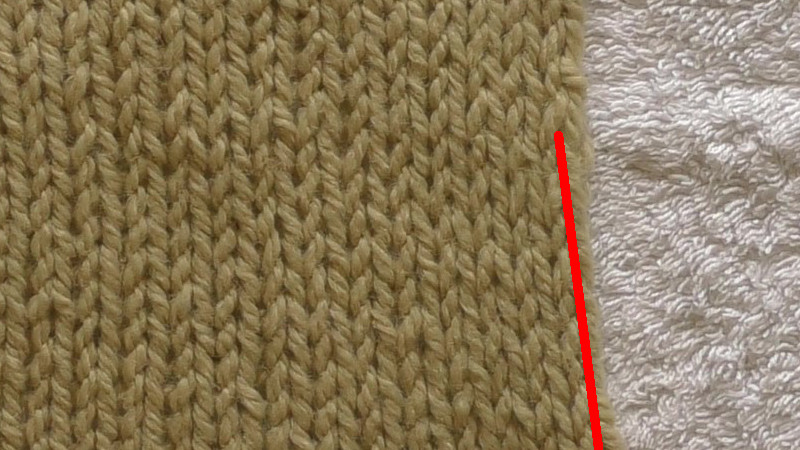 Swatch of stockinette stitch with the gap between the edge and next stitch highlighted. The edge stitch is curled to the side of the swatch.