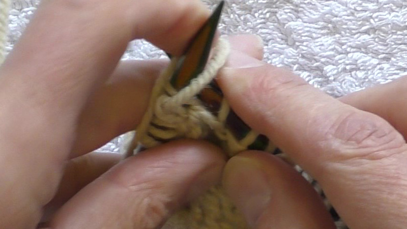 The working yarn is being wrapped around the left hand needle. It is being passed towards the right across the front of the needle before returning to the left behind the needle.