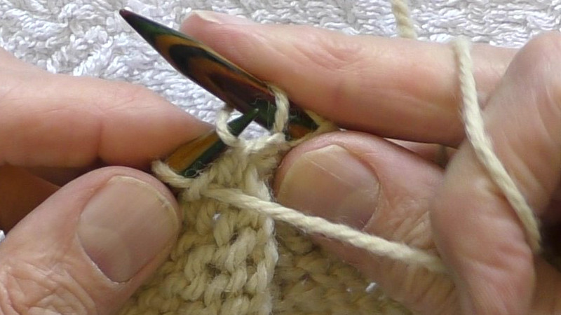 Tip of left hand needle being passed behind back leg of the stitch on the right hand needle and passed to the front through the centre of that stitch.