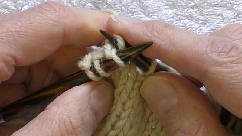 The new stitch is being pushed left onto the main body of the left hand needle. The right hand needle is being prepared to be pulled out of the old stitch.