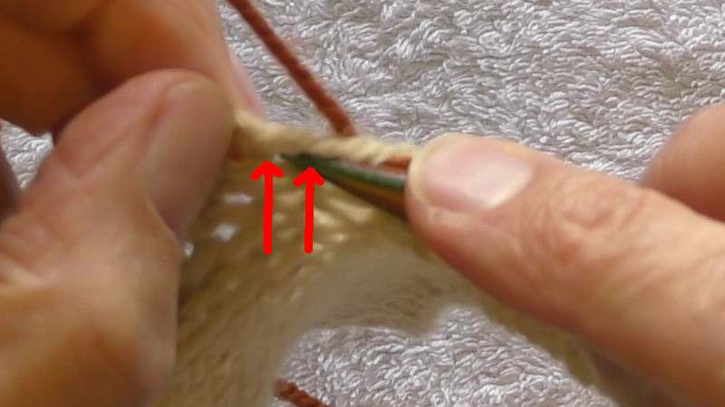 Needle being placed from front right to back left between two running threads of the original fabric. The running threads are highlighted by red arrows.