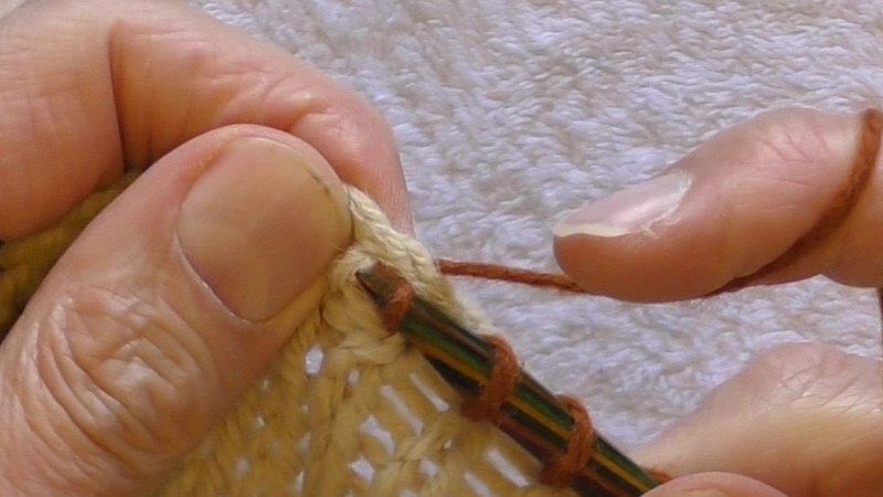 Yarn wrapped around a needle held in the right hand being pulled back towards the viewer through the stitch immediately below the cast-off edge so that a loop of yarn is made that passes through the middle of the stitch in the original fabric. The working yarn is held behind the fabric, and the new stitch formed by the loop is on the tip of the needle with "western" mount with the yarn at the front of the needle continuing (on the back of the fabric) to the previous stitch, and the yarn behind the needle forming the working yarn for the next stitch.