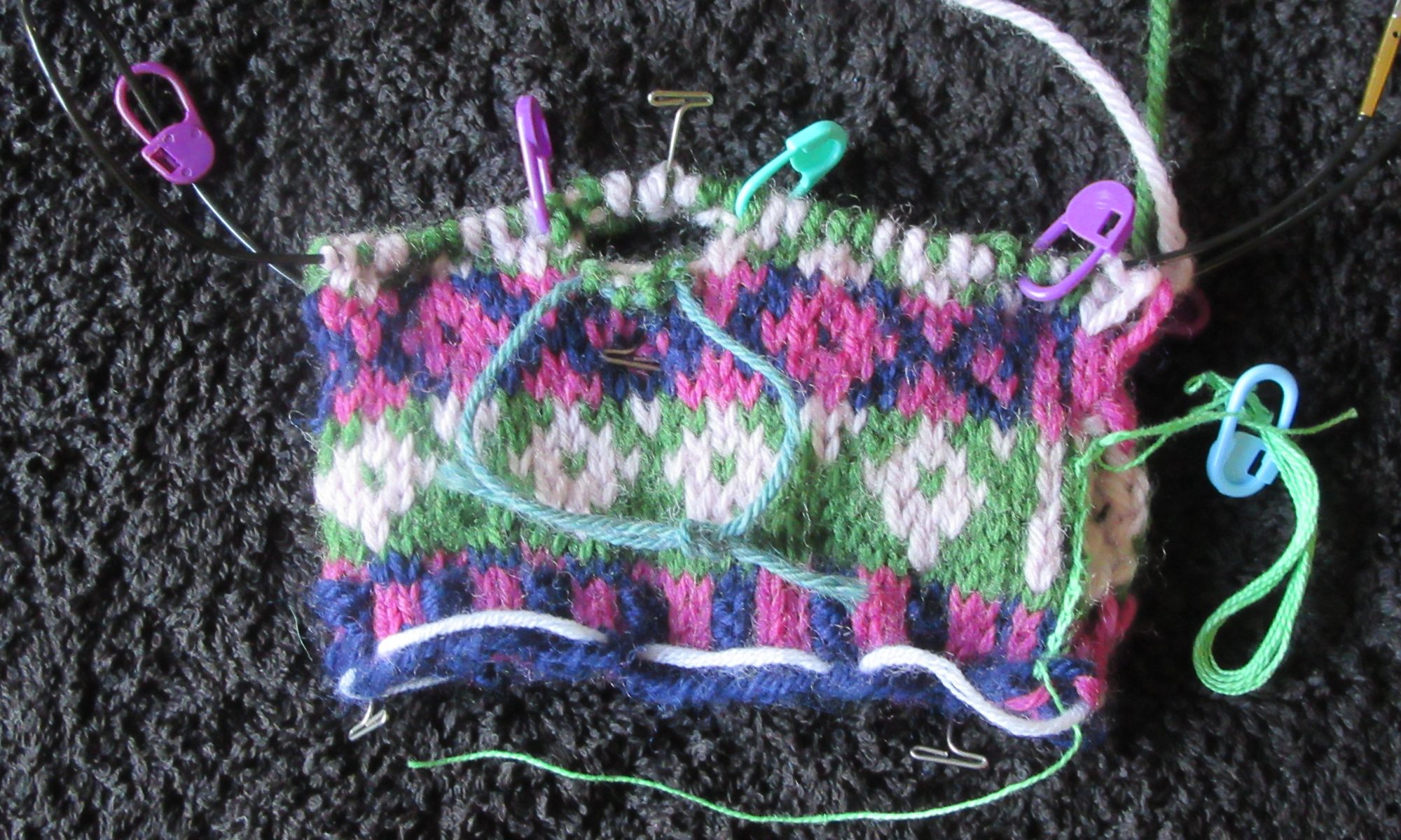 Stranded knitting showing how steeks have been cast on for armholes and stitches have been placed on a holder.